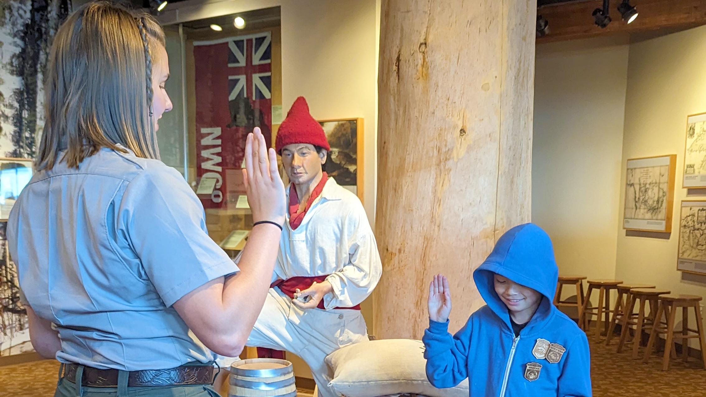 Uniformed NPS ranger with right hand raised facing a child in blue clothes with right hand raised.