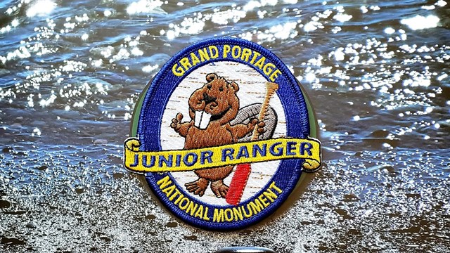 Embroidered beaver patch on a booklet cover showing water and a title.