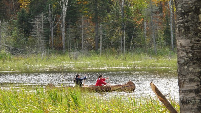 Two Ojibwe people paddling a birchbark canoe.