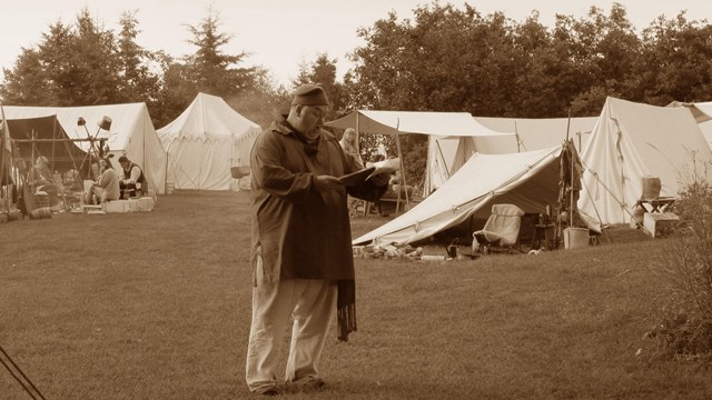 A sepia colored photo of a man in historic clothing, holding a clipboard.