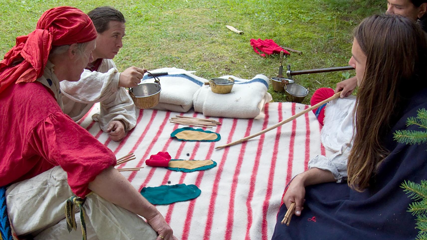 Four people lying down facing each other across a white blanket with red stripes and game pieces.