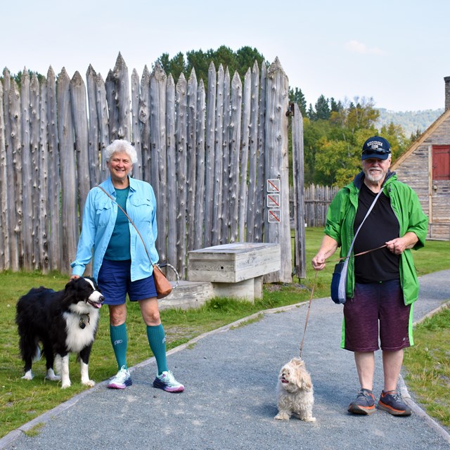 Two people with two dogs on leash, standing in front of a historic structure.