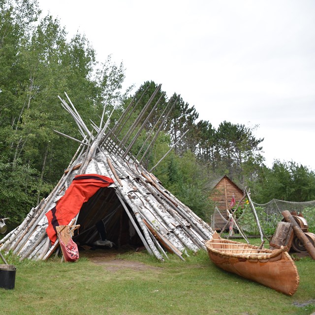 A birchbark wigwam and canoe with other tradition Anishinaabe items.