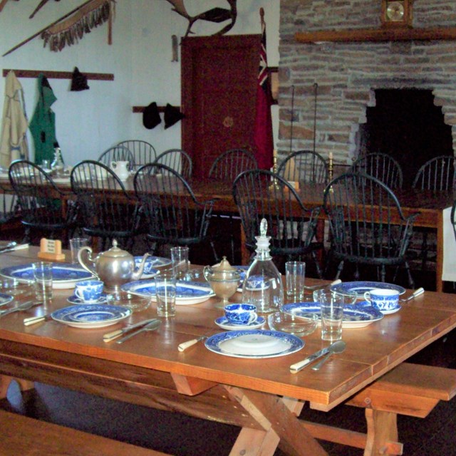A table set with historic blue and white china, glasses, and silver teapots.
