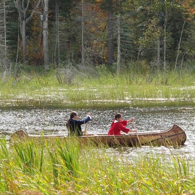 Two Ojibwe people paddling a birchbark canoe.