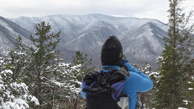 A hiker stands looking at snow-covered mountains.