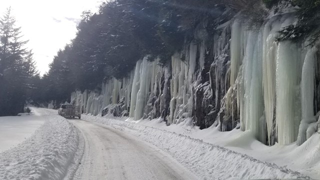 A snowy road with large icicles on the side.