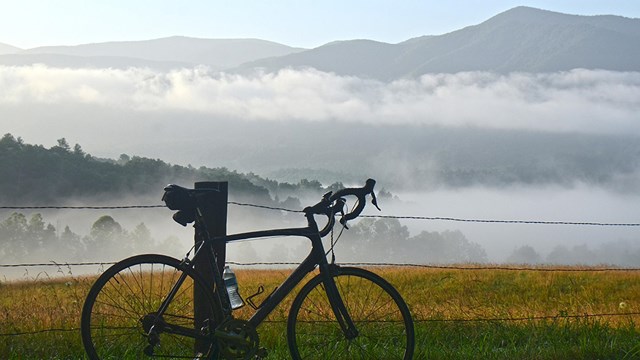 A bicycle leaning against a fence in Cades Cove. Misty mountains in background.