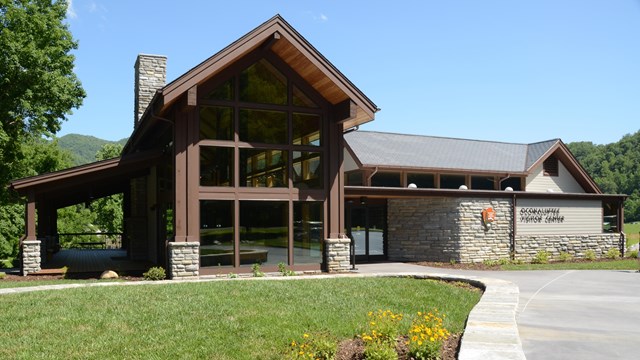 A building with many windows and a stone chimney. A grassy lawn with yellow flowers is in front.