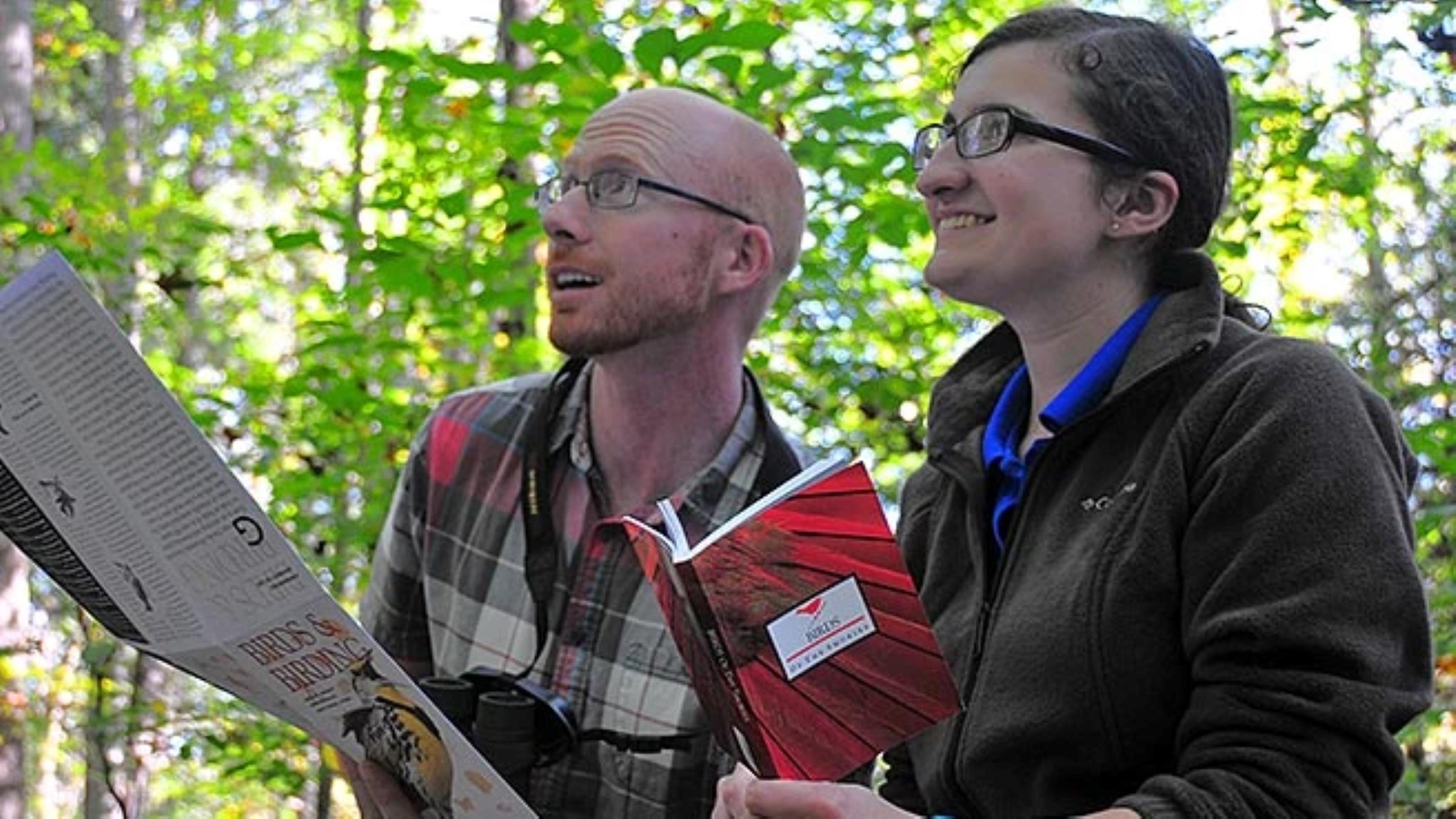 Two people standing in the woods with a map and bird book.