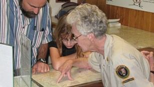 Two visitors, an adult and a child, look at a park map with a volunteer.