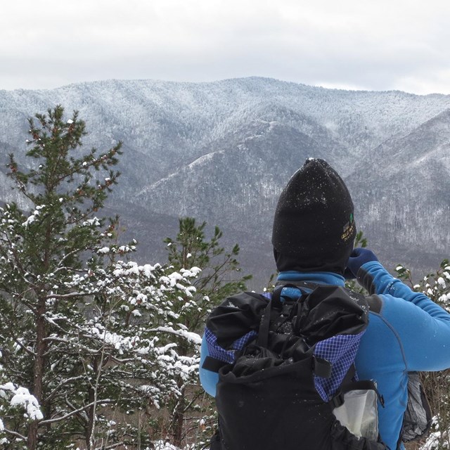 A hiker stands looking at snow-covered mountains.