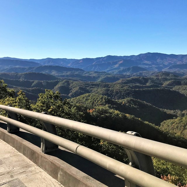 A bending roadway rail in the foreground of a blue-green colored mountain view