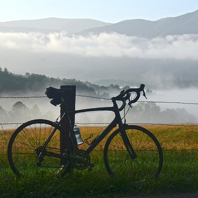 A bicycle leaning against a fence in Cades Cove. Misty mountains in background.