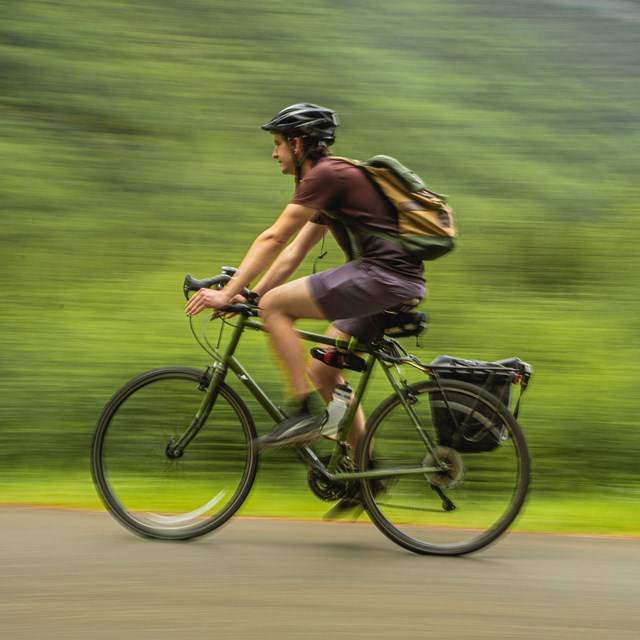 A man wearing a helmet bicycles on a path.