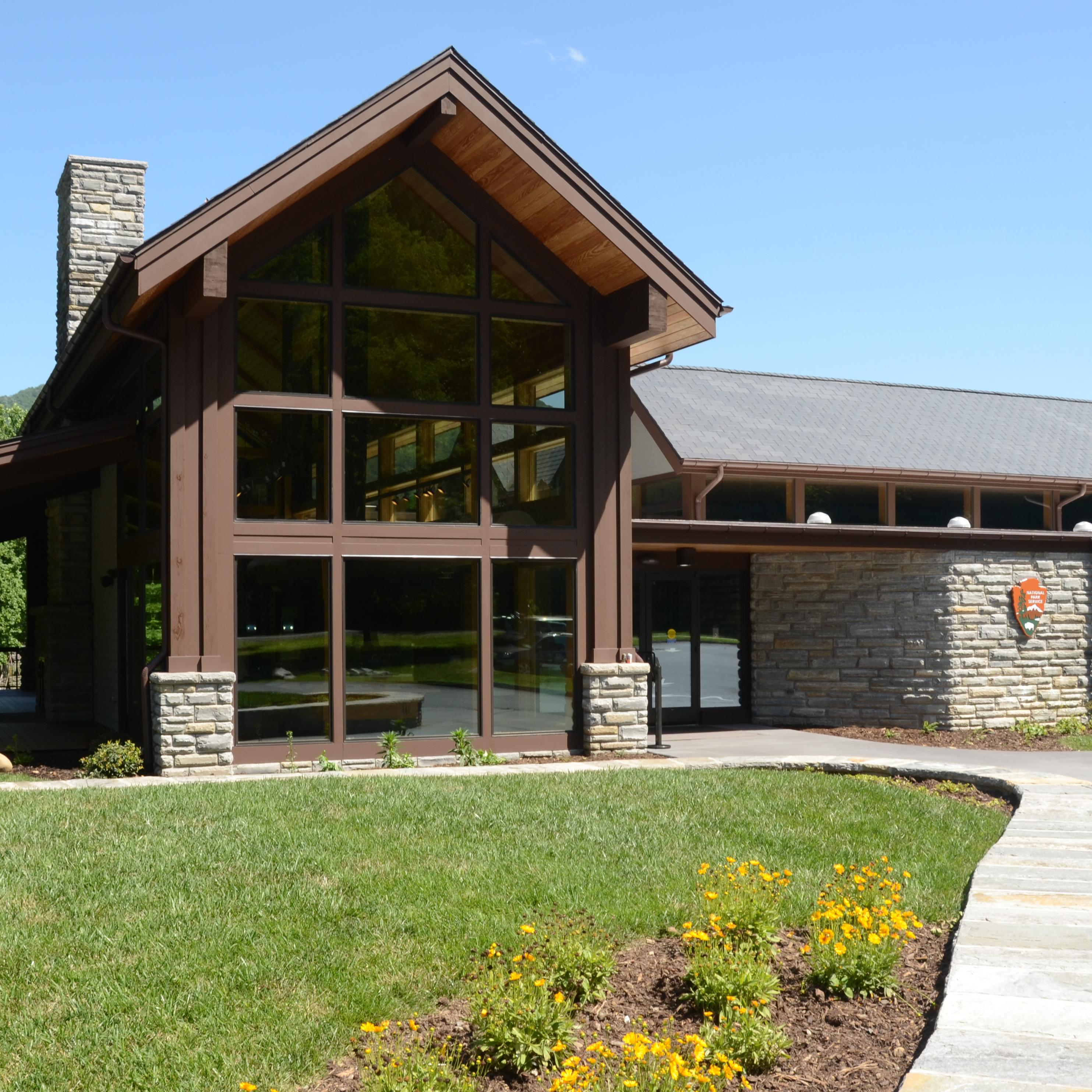 A building with many windows and a stone chimney. A grassy lawn with yellow flowers is in front.