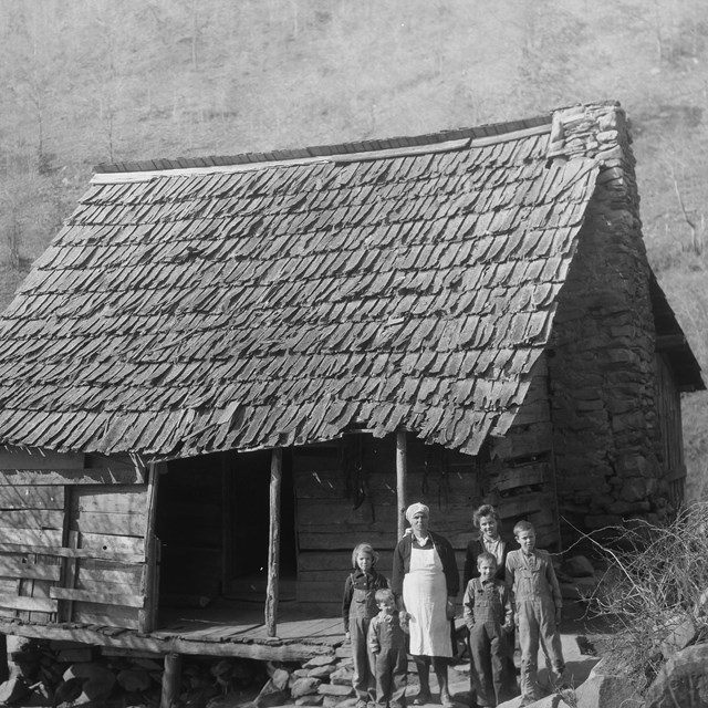 A log frame home with a family standing in the front, photo in black and white