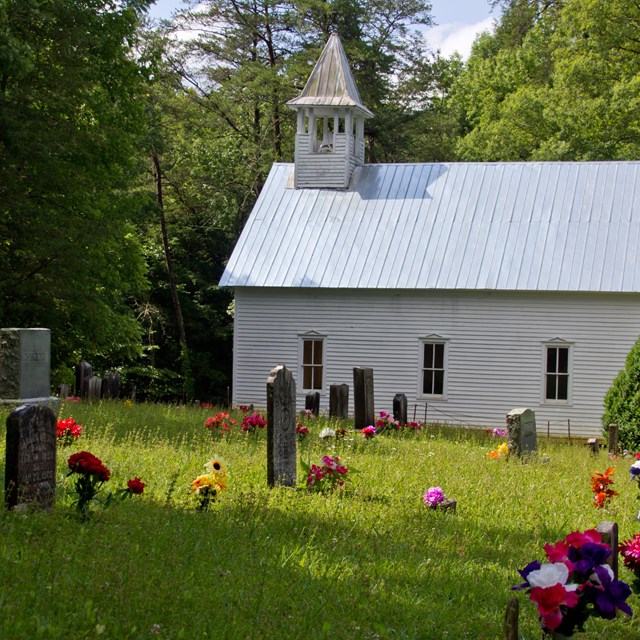 A grassy field with flower-decorated grave sites scattered in front of a white church building