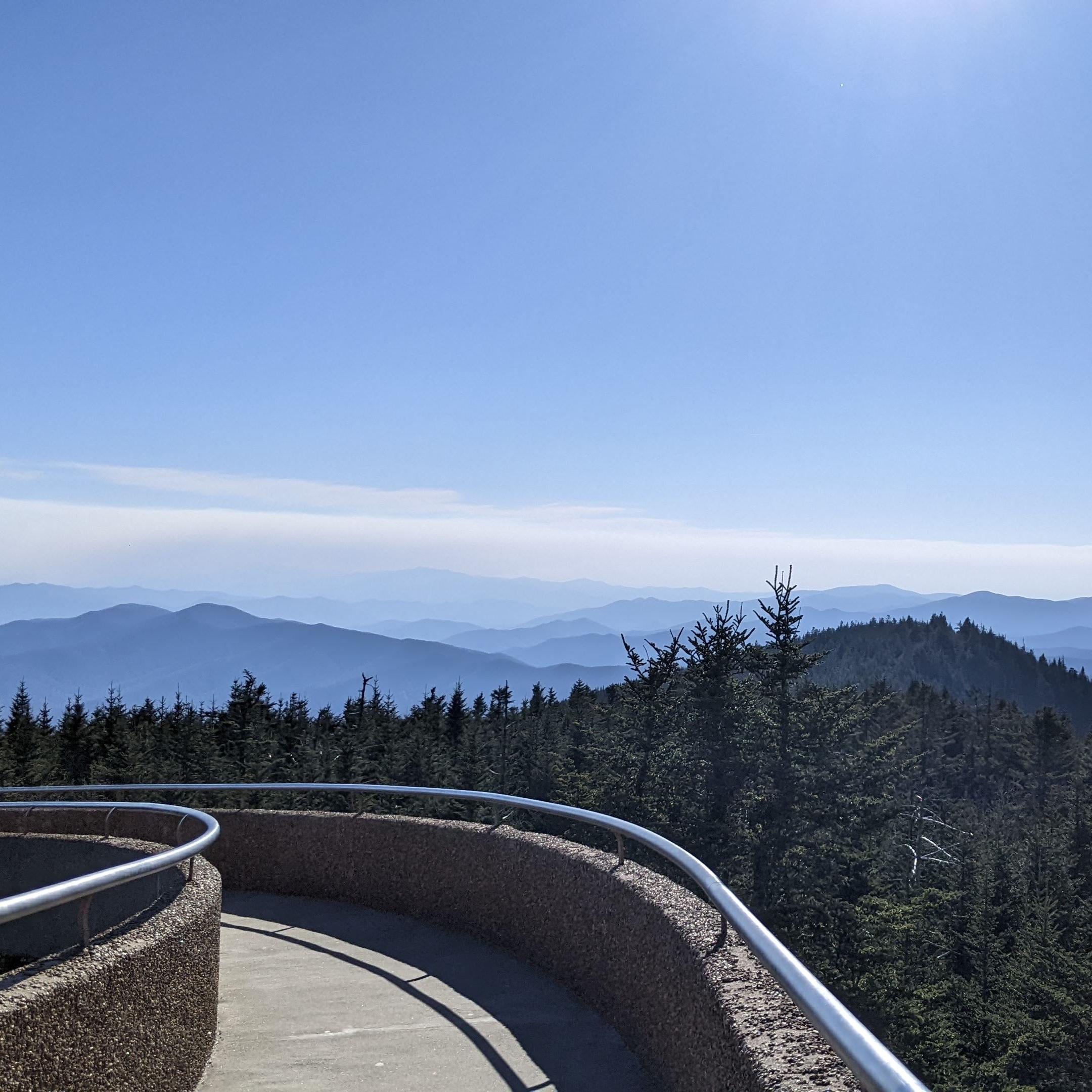 Sweeping mountain views in the distance. A paved walkway and trees in the foreground.