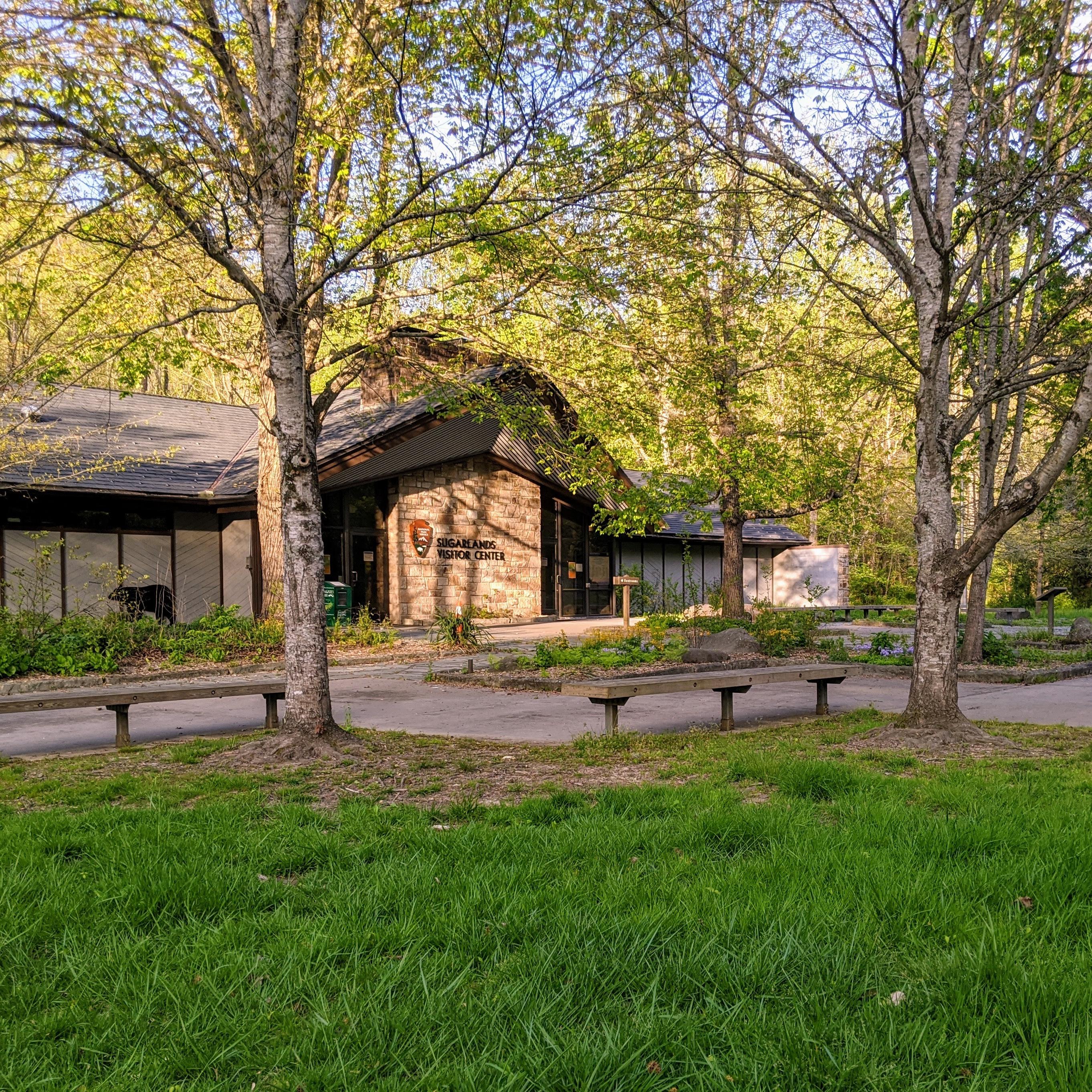 A visitor center with the NPS arrowhead on the building. Benches and paved walking areas in front.