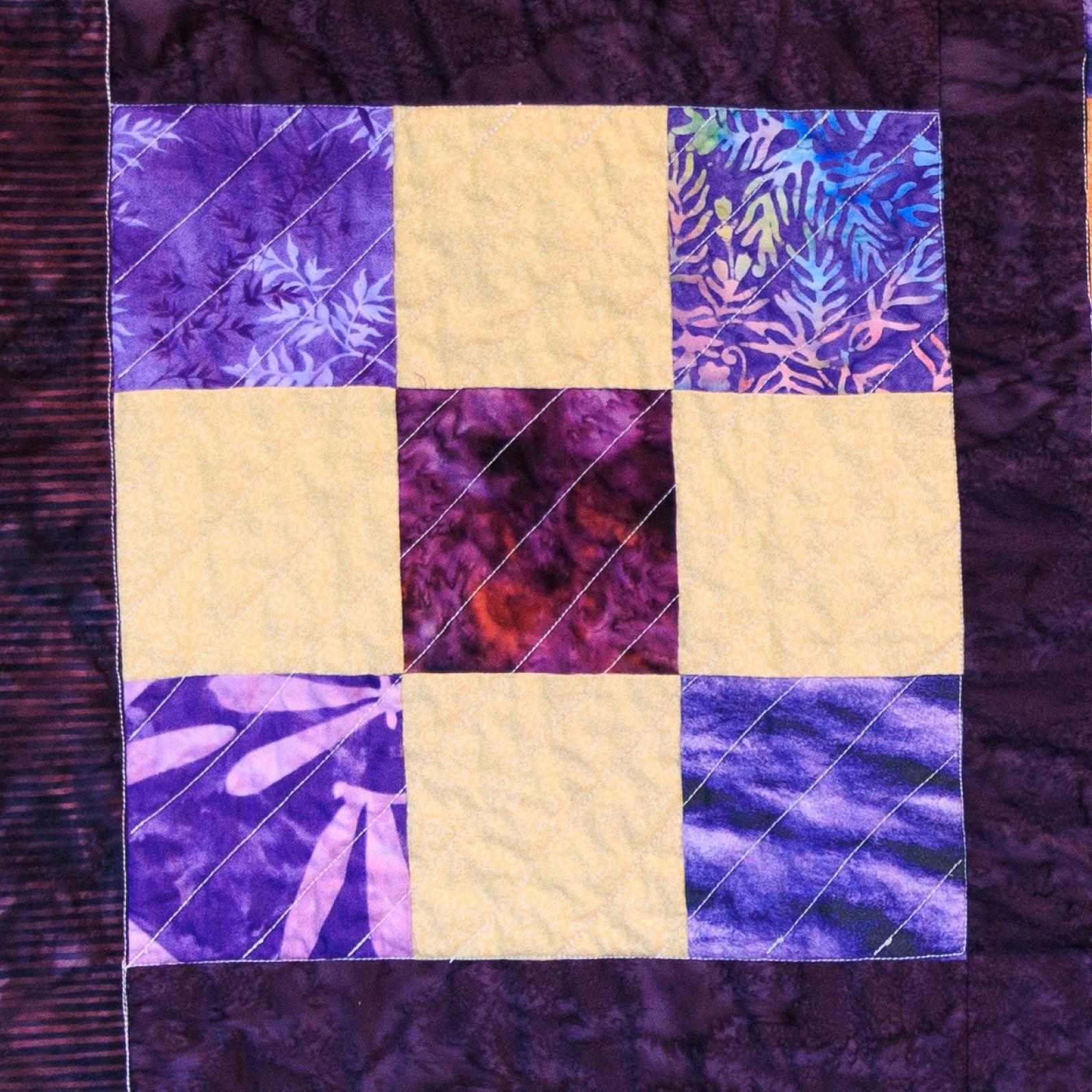 A square checkered quilt block that is purple and yellow.