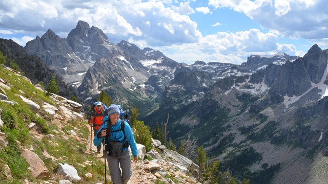 Two backpackers hiking up trail with the Grand Teton in the distance.