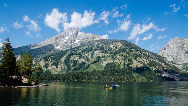 A canoe floats on a lake at the base of a mountains.