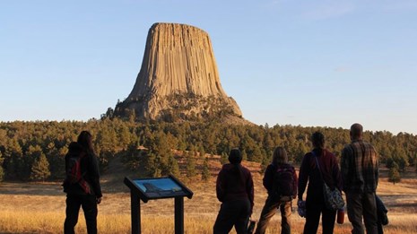 Devils Tower, a large rock monolith extending into the sky with visitors in foreground