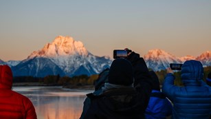 Visitors watch the sun rise on mountains.