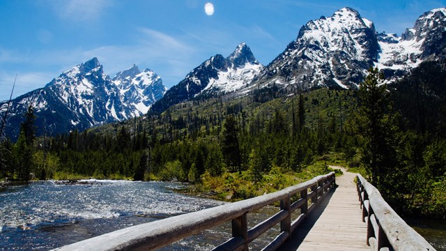 A wooden bridge crosses a creek towards mountains