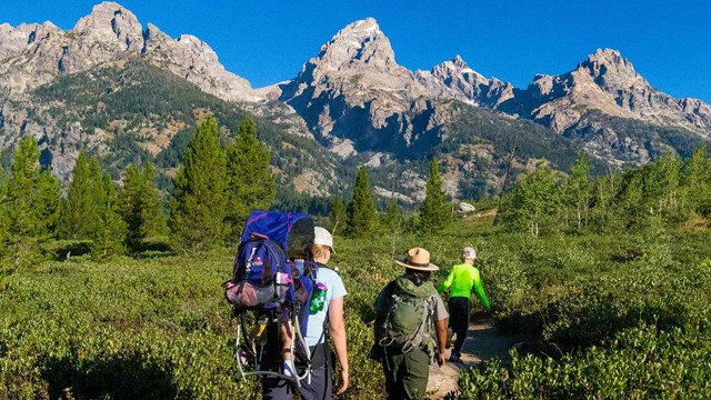 A group of people hiking with a Ranger with the Grand Teton in the distance.