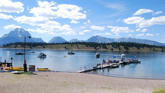 A dock with multiple boats on a lake with mountains in the background.