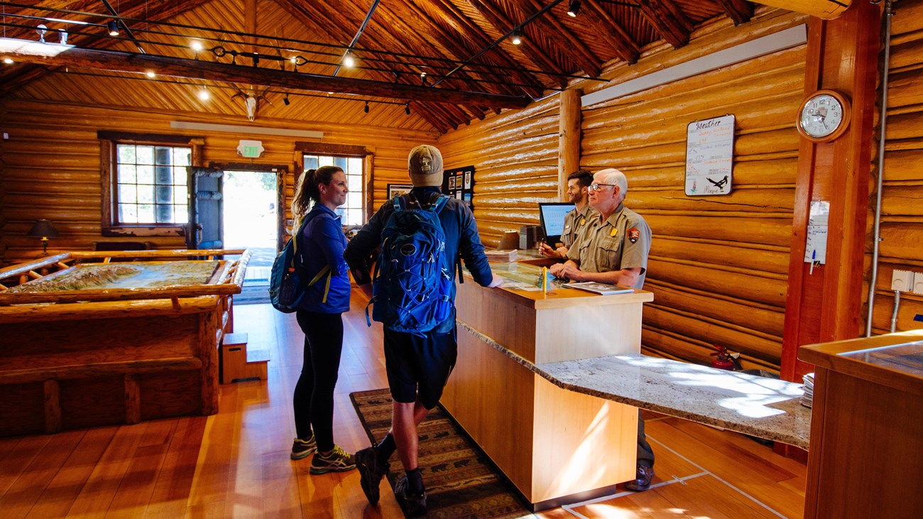 Visitors talk to rangers in a log cabin.
