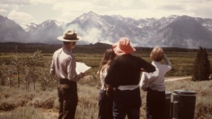 A ranger talks with three visitors about the fire visible in the distance.