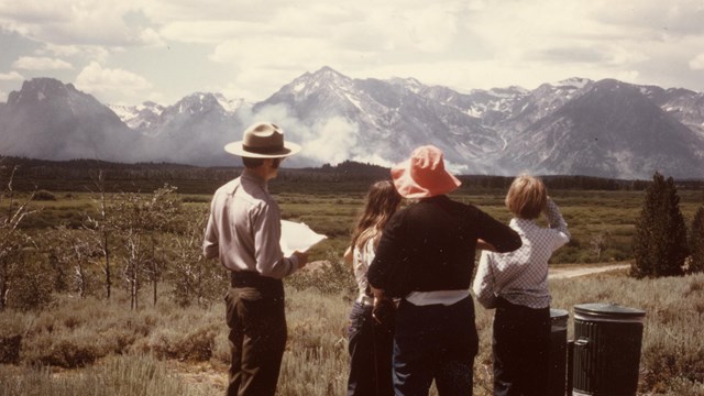 A ranger talks with three visitors about the wildfire in the distance.