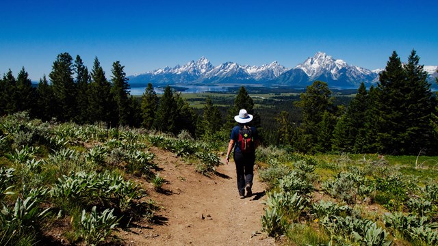 A hiker walks down a trail towards distant mountains.