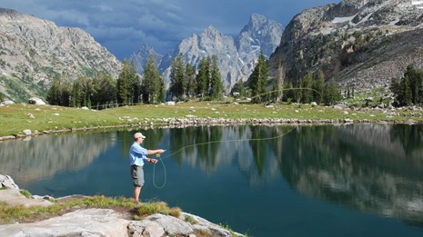 A man fly fishes at an alpine lake