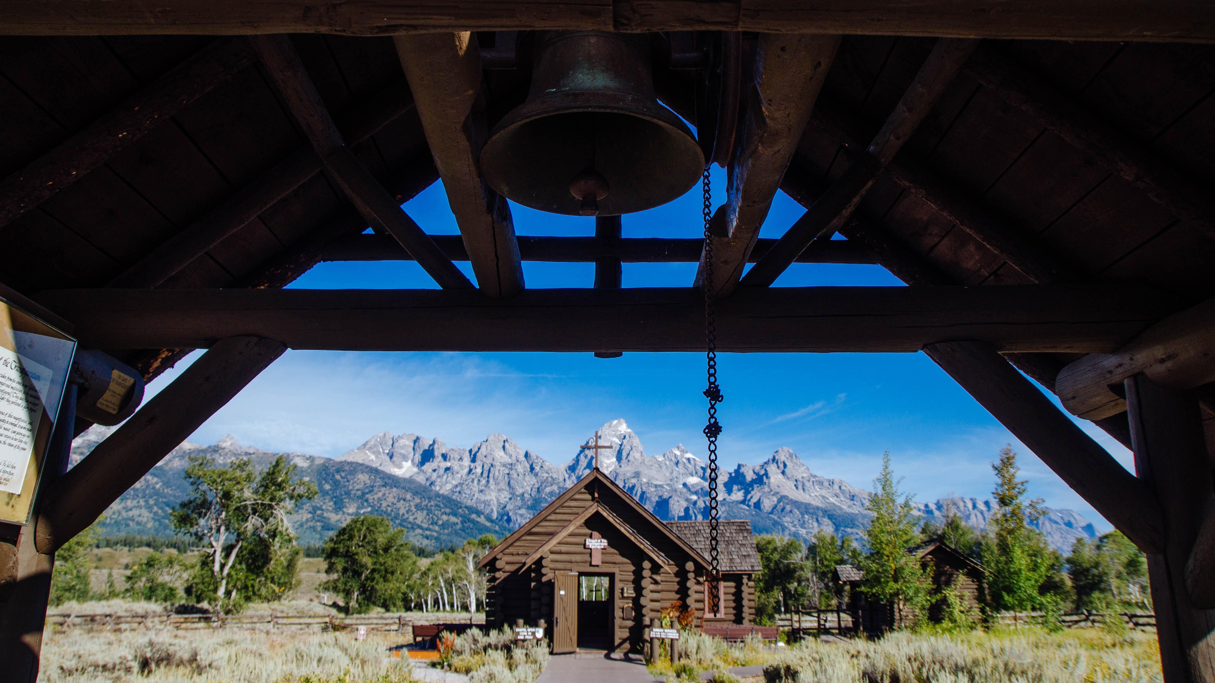 A bell in front of a wood chapel.