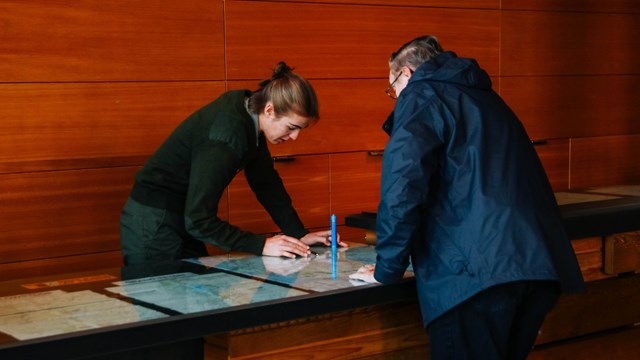 A ranger stands behind a desk talking to a visitor.