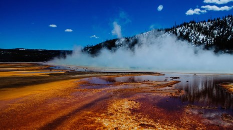 Steam rises off a brightly colored pool.