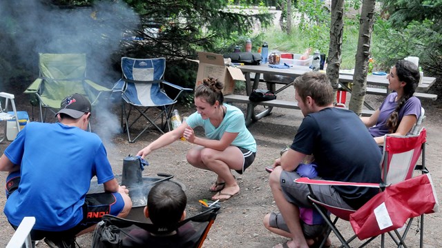 5 people sit around a campfire