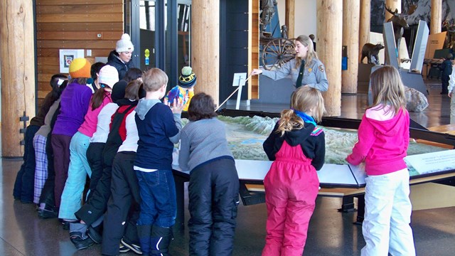 A park ranger teaches a group of students about Grand Teton using a large raised relief map