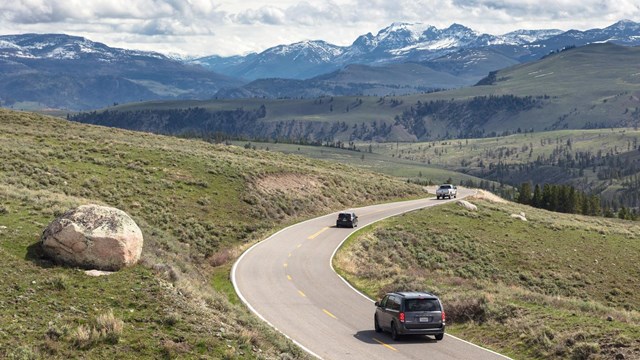 Cars driving on winding road in a sage covered valley.