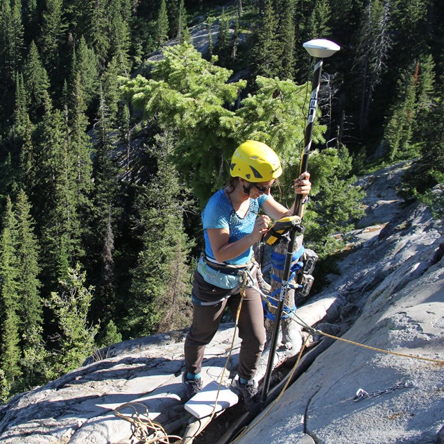 A researcher is roped up to place equipment on a steep rock face.