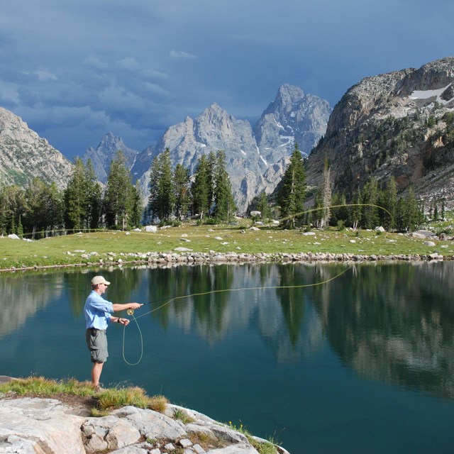 A man fly fishes at an alpine lake