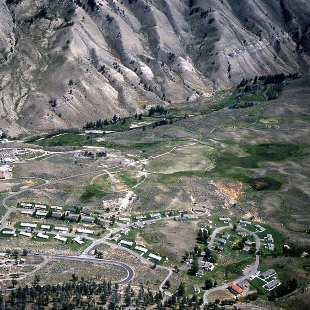 Overhead view of roads and houses adjacent to undeveloped land at the base of mountains.