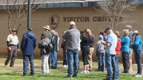 Visitors gather around tour guide and limestone monument on guided tour.