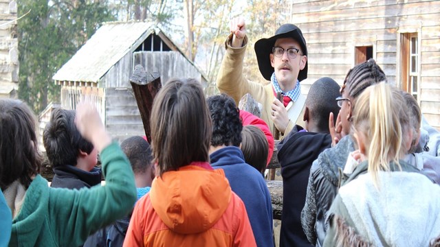 Living history militiaman points at student raising their hand. Other students crowd around.