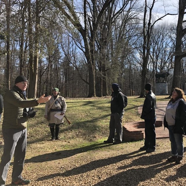 A group of people look at a presenter on a battlefield