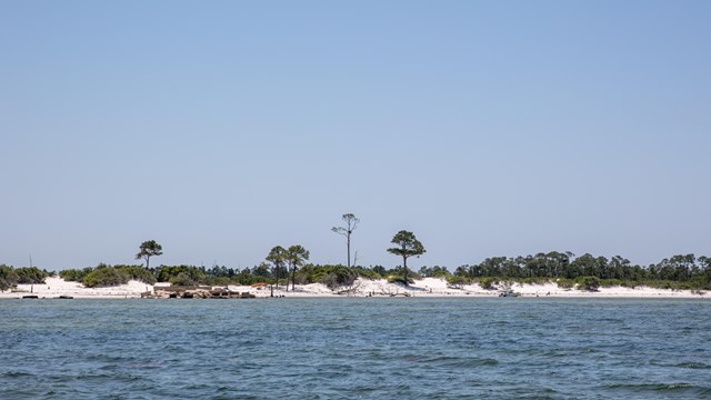A remote island with sparse vegetation is seen from the water.